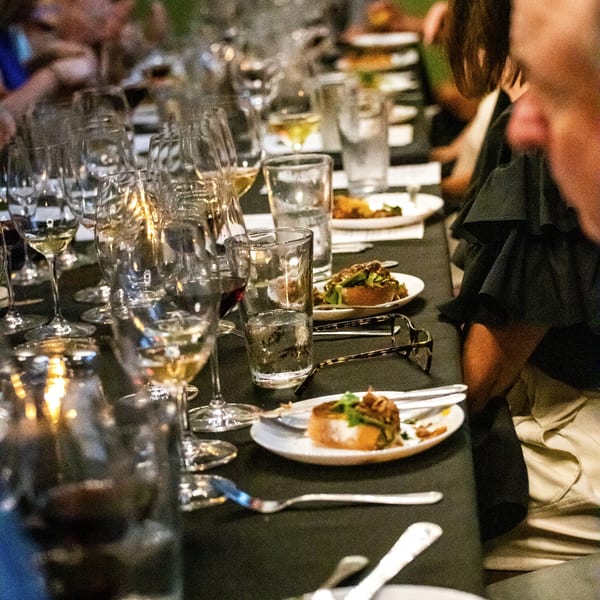 Guests seated at a long table with wine glasses, water glasses, and small plates of Italian appetizers.