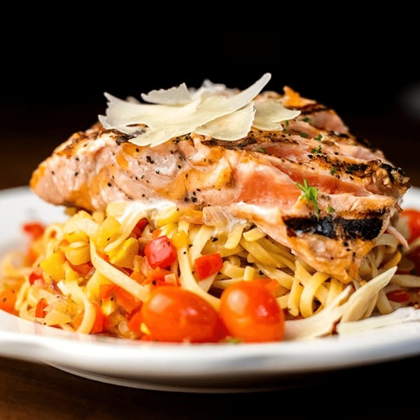 Grilled salmon with shaved parmesan, served over linguine pasta with cherry tomatoes and vegetables.
