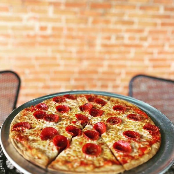 A Pignetti's pepperoni pizza on a metal tray, with a brick wall in the background.