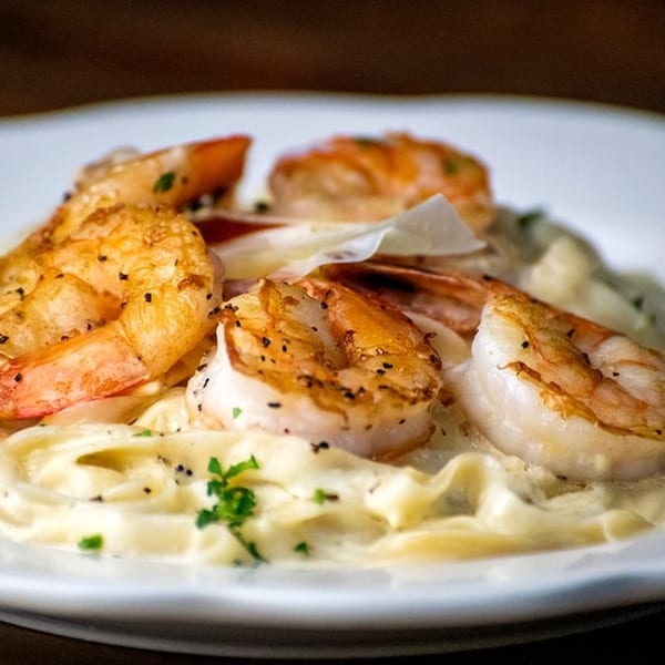 Pignetti's shrimp scampi with fettuccine pasta, creamy sauce, and fresh parsley on a white plate.
