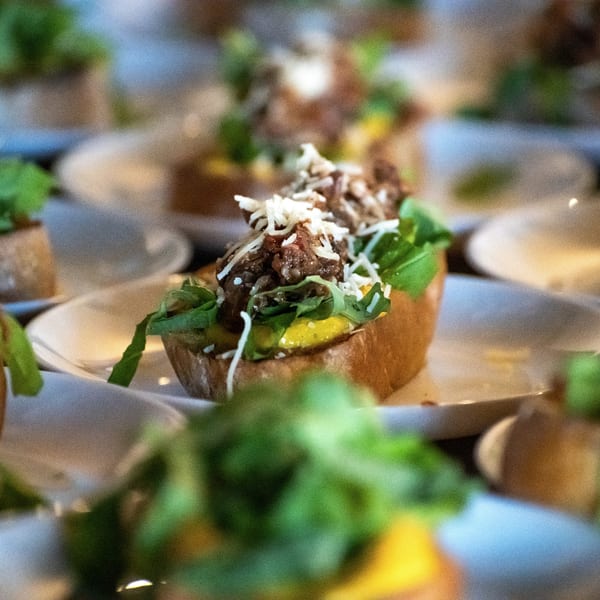 Close-up of a Pignetti's bruschetta with beef, arugula, and shredded cheese on a white plate.