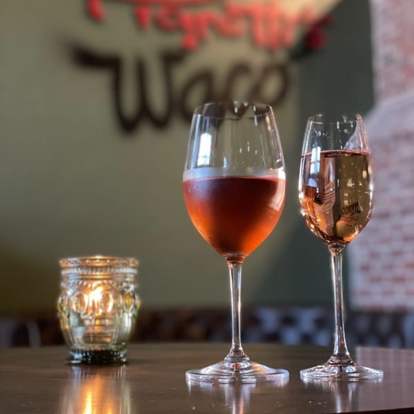 Two glasses of rosé wine and a flickering candle on a table at Pignetti's Waco.