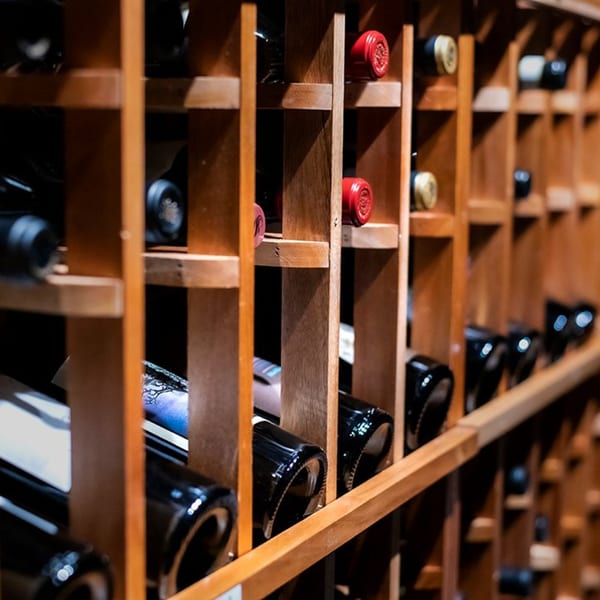 Rows of wine bottles with red and gold foil tops stored in a wooden rack at Pignetti's.