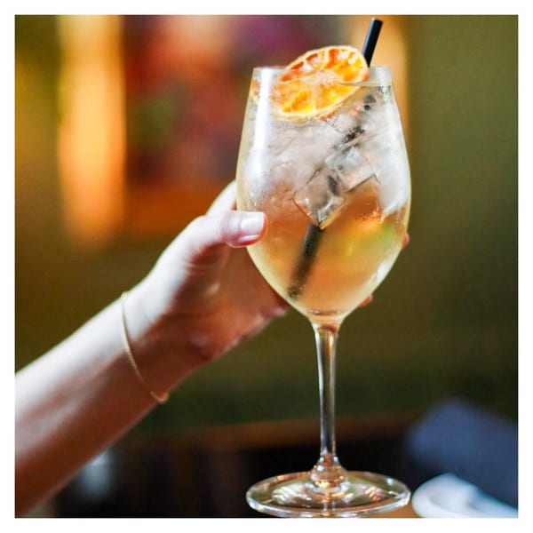 A hand holds a Pignetti's Italian restaurant cocktail with ice, a dried orange slice, and a black straw.