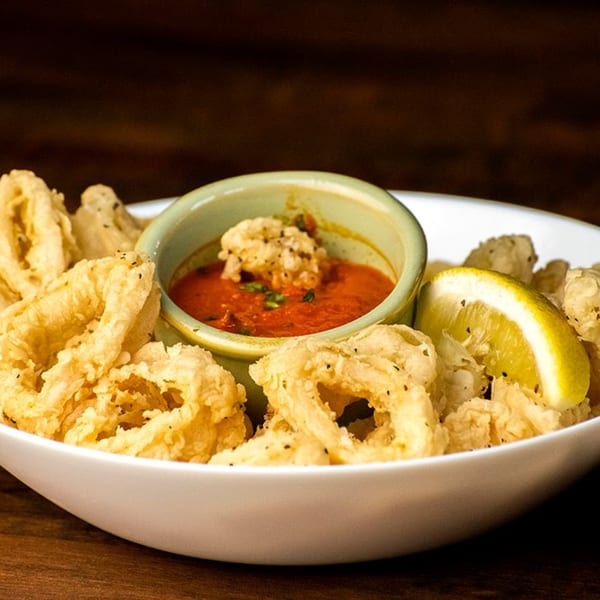 Crispy fried calamari rings with a side of red marinara sauce and a lemon wedge.