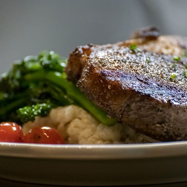 Close-up of a Pignetti's Italian dish with seared meat, broccoli, cherry tomatoes, and mashed potatoes.
