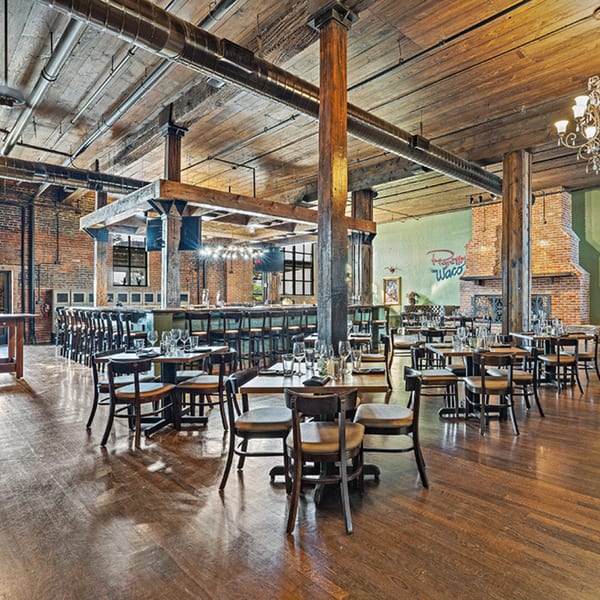 Pignetti's Waco dining room with wooden tables, chairs, a bar, and exposed brick walls.