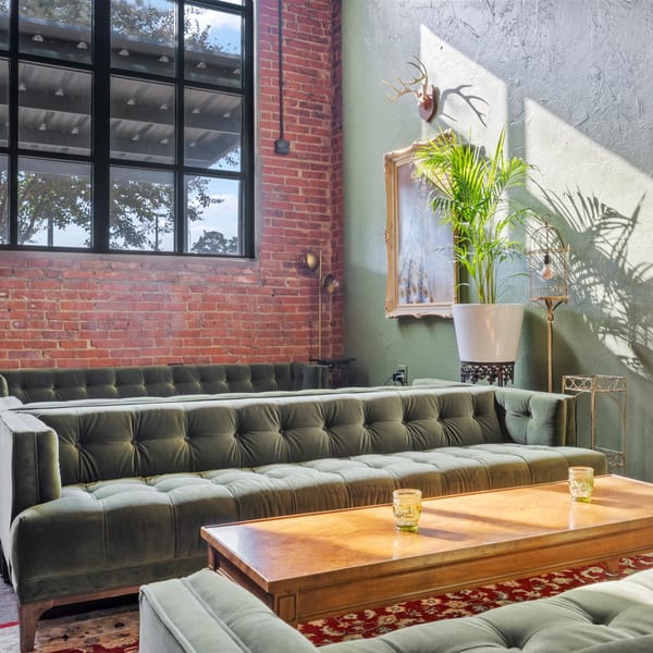 Pignetti's lounge area with green velvet sofas, a wooden coffee table, and brick walls.