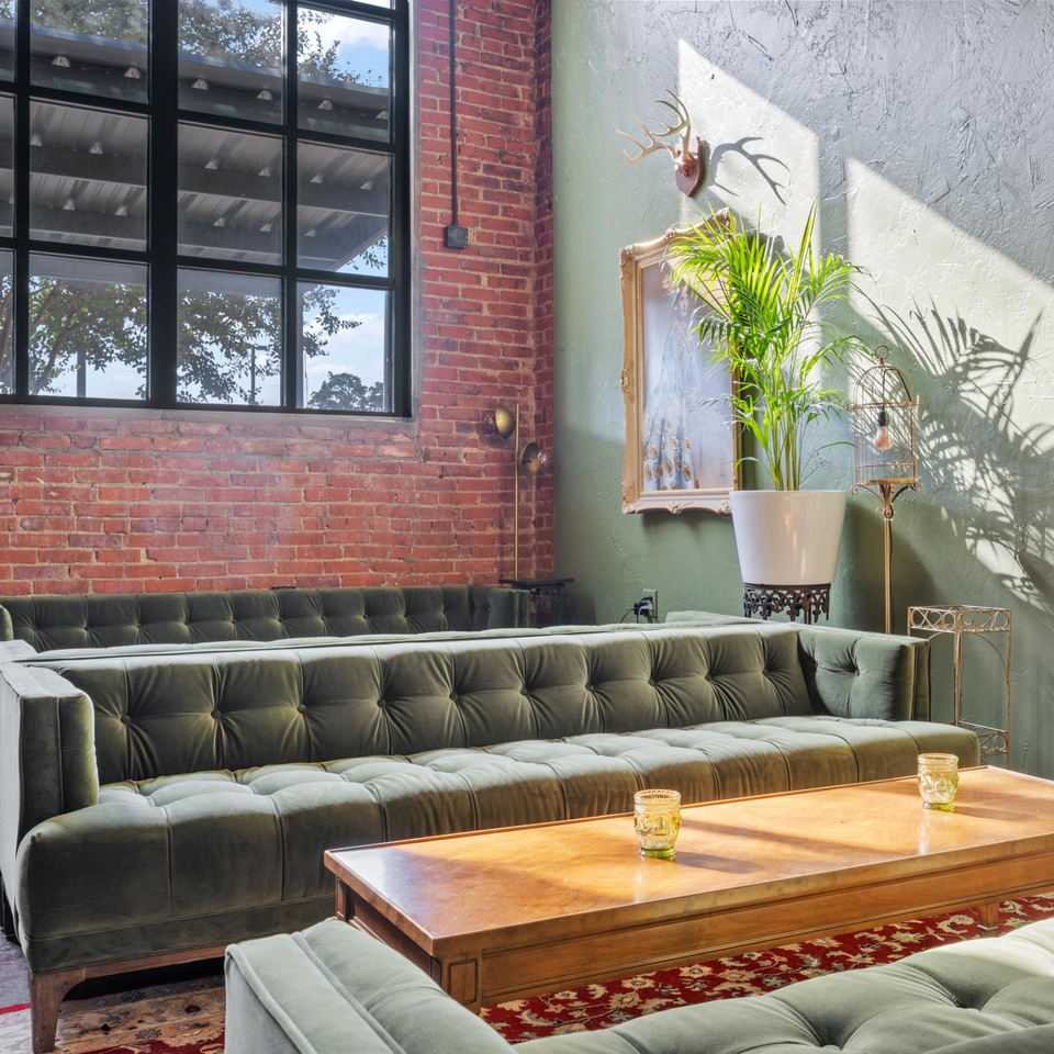 Pignetti's lounge area with green velvet sofas, a wooden coffee table, and brick walls.