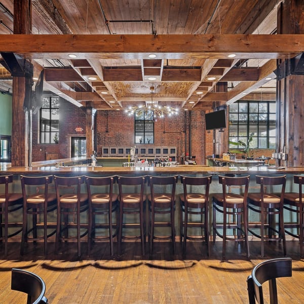 Pignetti's Waco bar area with wooden stools, exposed brick, and a large chandelier.