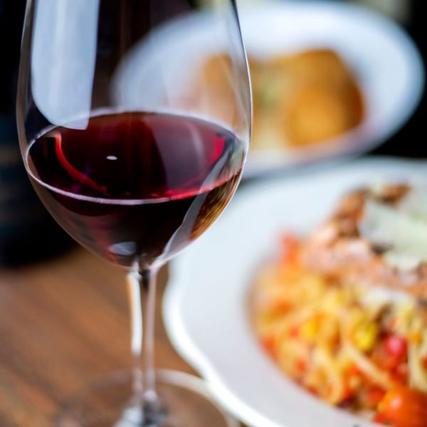 A glass of red wine with Italian pasta and another dish blurred in the background at Pignetti's.